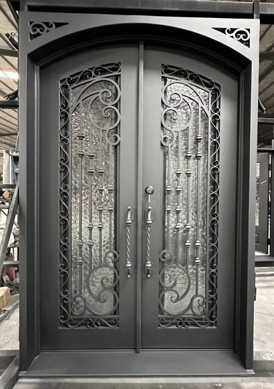Elegant double iron doors with glass panels, featuring ornate scrollwork and vertical bars in a symmetrical design. The doors have arched tops, decorative handles, and a dark matte finish.