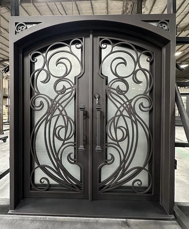 Double wrought iron doors with ornate, swirling designs and frosted glass panels, set in a robust dark metal frame. The doors are located indoors, with industrial ceiling and beams visible in the background.