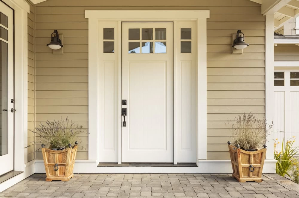 A beige house exterior with a white front door, sidelights, and transom windows. Two large wooden planters with dried lavender flank the entrance. For a stunning upgrade, consider custom iron doors Middlesex & Bergen County.