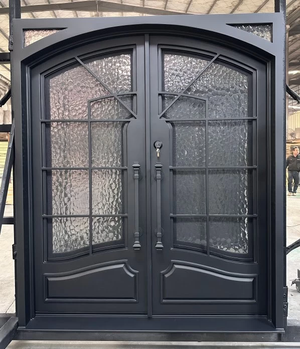 Black double entry doors with decorative glass panels and arched transom, featuring intricate metalwork and textured glass, set in an industrial warehouse environment.